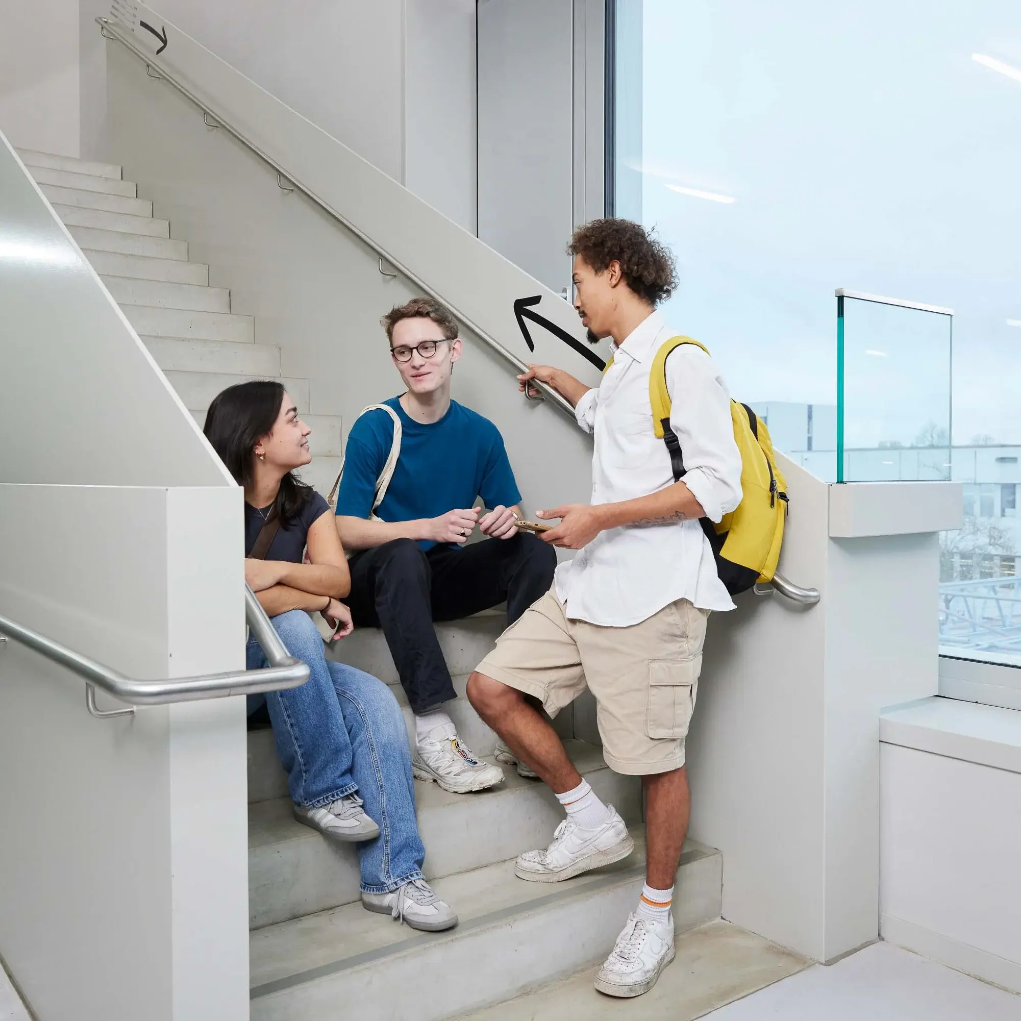 Studierende sitzen auf der Treppe und unterhalten sich.
